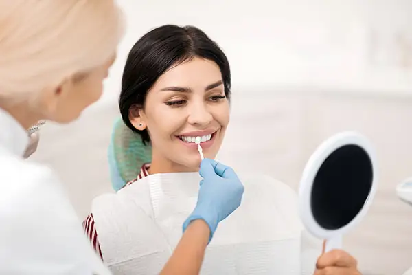 Female patient smiling while a dentist helps her select a shade for dental veneers using a color guide in a modern dental clinic.